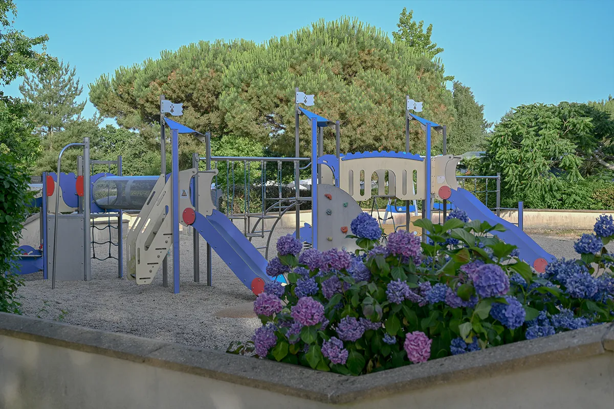 aire jeux enfants hortensias Structure de jeux avec toboggan tunnel et mur d'escalade, bordée d'hortensias bleus et roses
