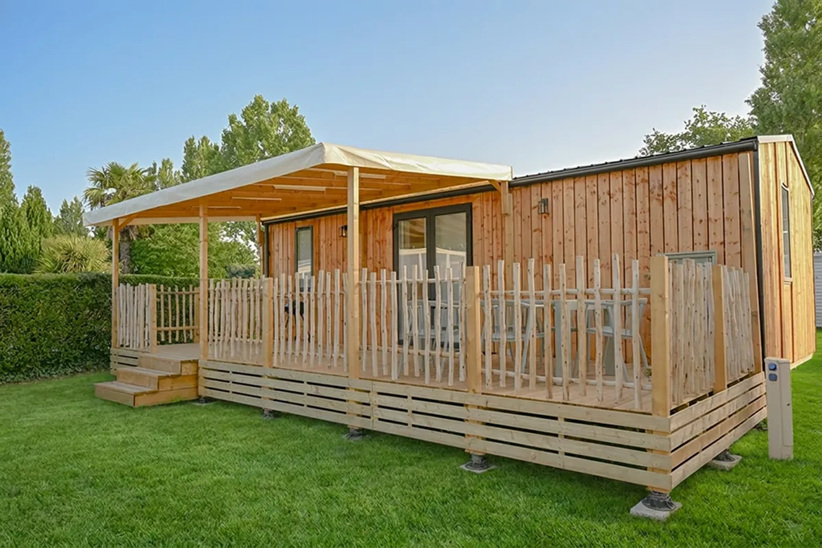 mobil home bois terrasse gazon Mobil-home à bardage bois avec terrasse couverte et clôture en bois, installé sur pelouse