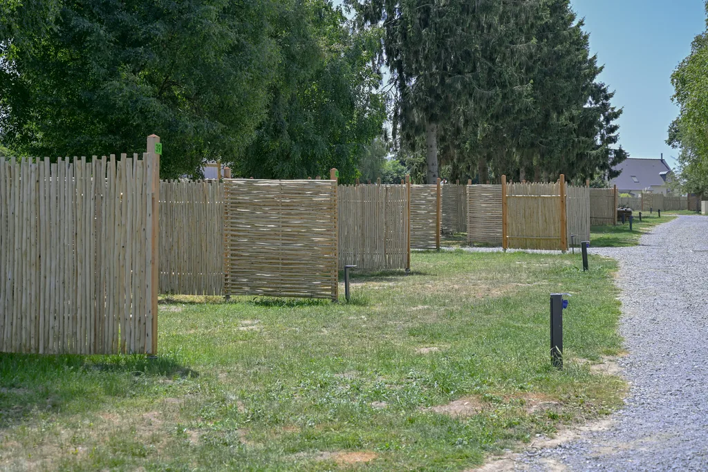 palissades emplacements nus camping Rangées de palissades en châtaignier tressé délimitant des emplacements nus le long d'une allée de gravier